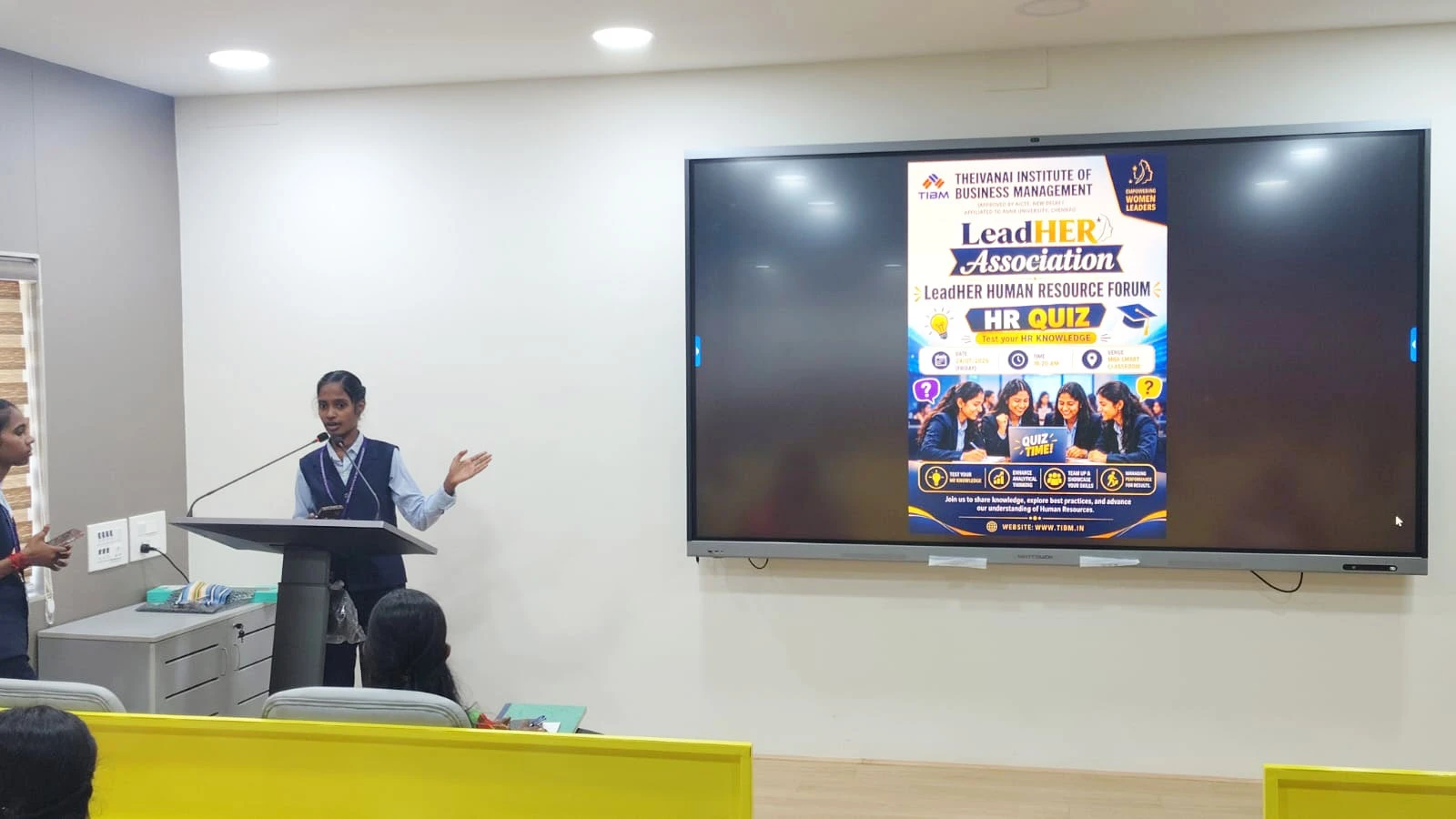 Two organisers introducing the HR Quiz in the smart classroom, with the quiz poster on the screen